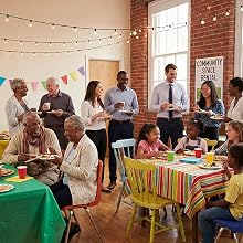 Text reads: 'COMMUNITY SPACE RENTAL'. Indoor gathering with colorful striped tablecloths, string lights, and bunting decorations. People seated at tables in brick-walled room.